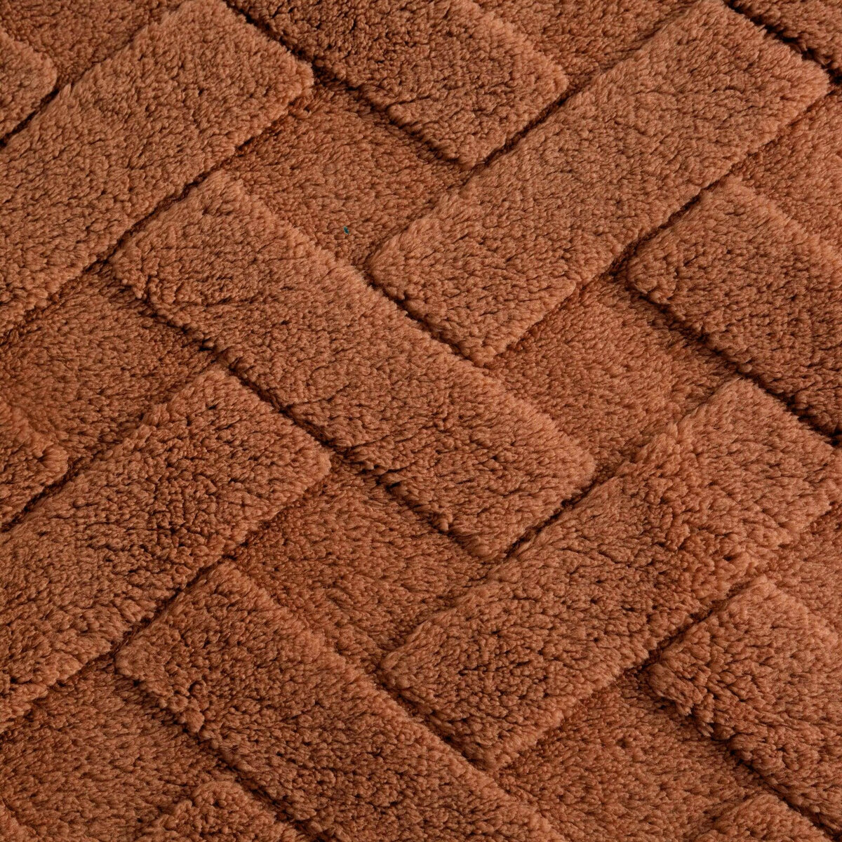 Obraz przedstawia teksturę pluszowego materiału w kolorze ceglastym, ułożoną w wzór jodełki.