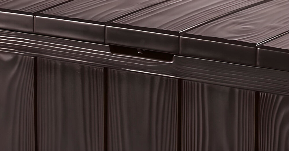 Zbliżenie na brązową skrzynię ogrodową z fakturą przypominającą drewno. Widoczna jest część pokrywy z uchwytem.