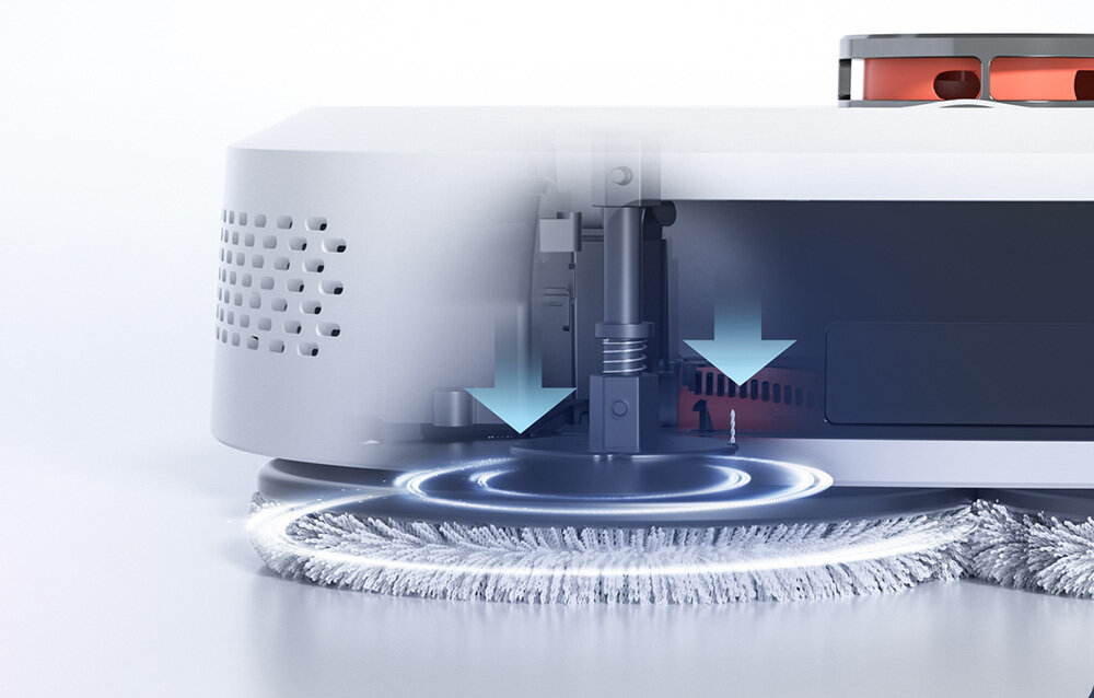 Obraz przedstawia zbliżenie na dolną część robota sprzątającego z widocznymi szczotkami i strzałkami wskazującymi ruch w dół. Widać także perforowane otwory na obudowie urządzenia.