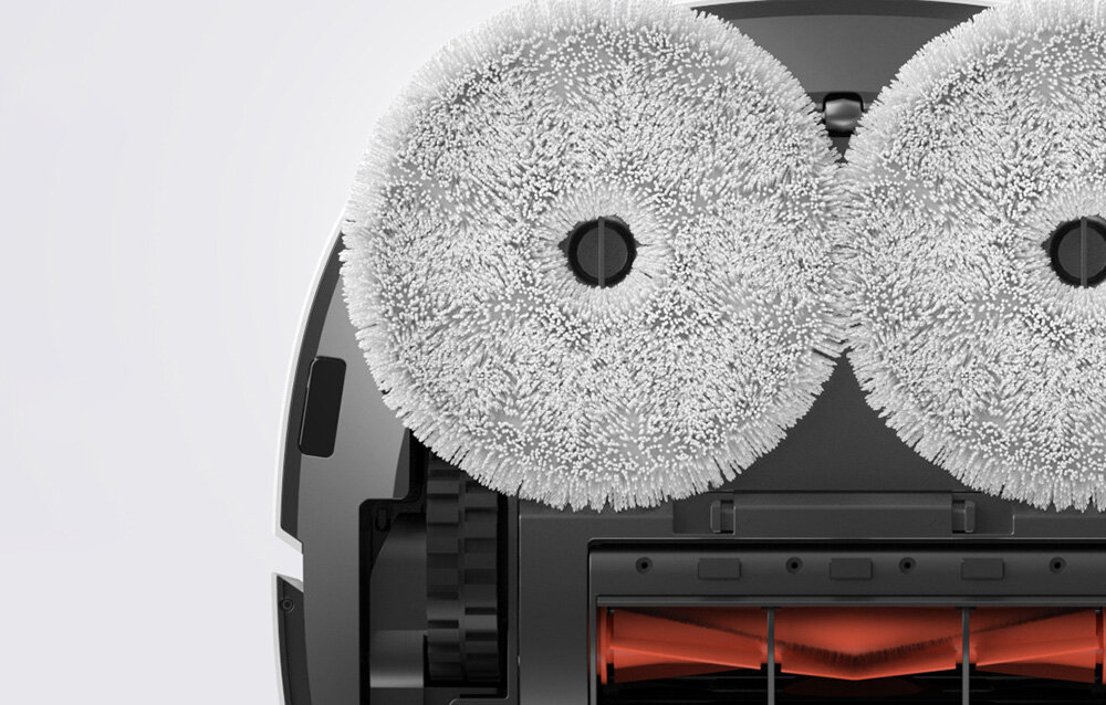 Obraz przedstawia dolną część robota sprzątającego z dwoma okrągłymi, białymi szczotkami. Widoczne są również elementy mechaniczne i szczotka w kolorze pomarańczowym.