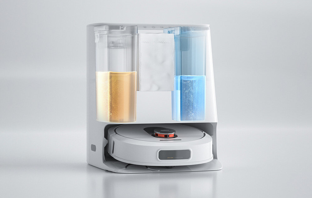 Na obrazie widoczny jest robot sprzątający umieszczony w stacji dokującej z dwoma przezroczystymi pojemnikami na płyny po bokach. Robot ma okrągły kształt i biały kolor.