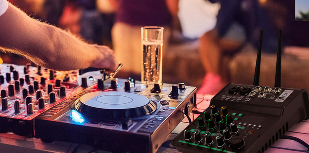 Na obrazie widać osobę obsługującą sprzęt DJ-ski z mikserem audio i konsolą. Obok znajduje się mikser audio z kilkoma pokrętłami i wskaźnikami świetlnymi.