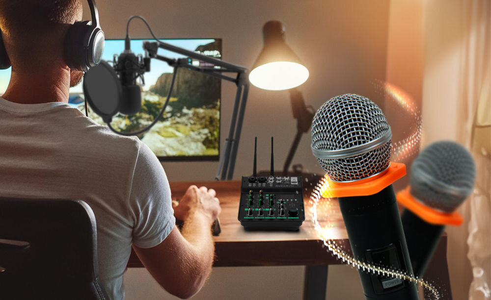 Osoba siedzi przy biurku z komputerem, na którym wyświetlany jest krajobraz. Na pierwszym planie widoczne są dwa mikrofony oraz mikser audio z różnymi pokrętłami i przyciskami.