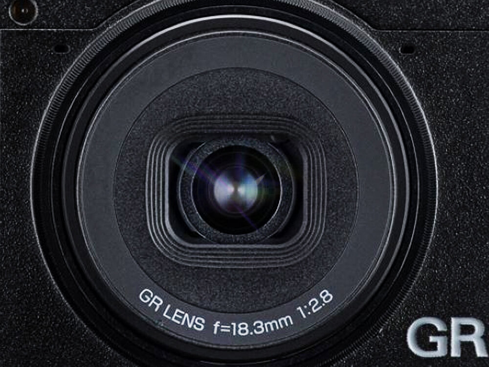 Zbliżenie na obiektyw aparatu z widocznym napisem \'GR LENS f=18.3mm 1:2.8\'.