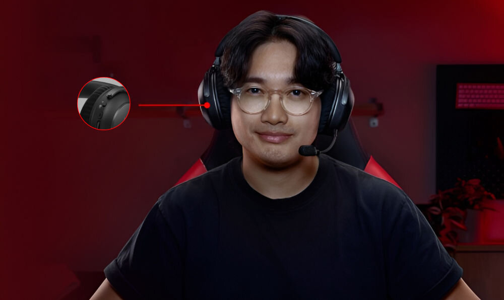 Osoba nosi nauszne słuchawki z mikrofonem, siedząc na krześle gamingowym. W tle widoczne jest rozmyte oświetlenie i elementy wyposażenia pokoju.