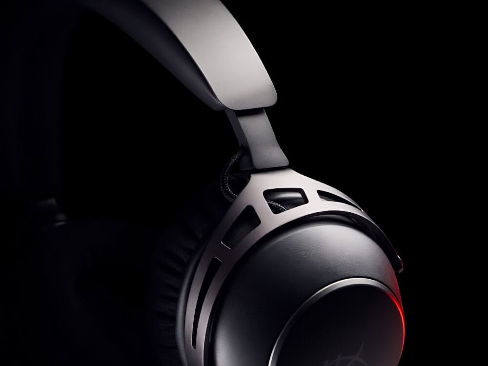 Zbliżenie na nauszną część słuchawek z metalowym pałąkiem i czarną poduszką. W tle widoczny jest ciemny, jednolity kolor.