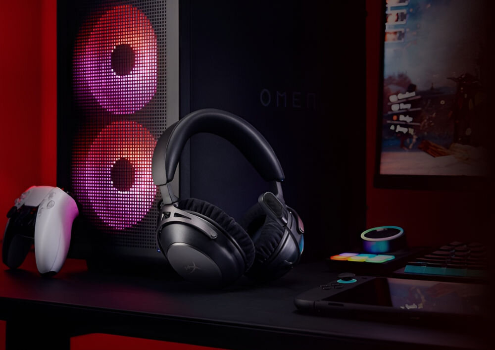 Na biurku znajdują się czarne słuchawki nauszne, obok których stoi konsola do gier i komputer z podświetleniem RGB. Na obudowie komputera widoczne jest logo \'OMEN\'.