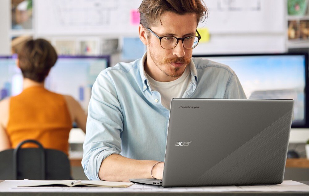 Laptop ACER Chromebook Plus 514 CB514-3H-R36J Mężczyzna siedzący przy biurku w jasnym pomieszczeniu pracuje na srebrnym laptopie z widocznym napisem 'chromebook plus' i logo 'acer' na pokrywie, opis