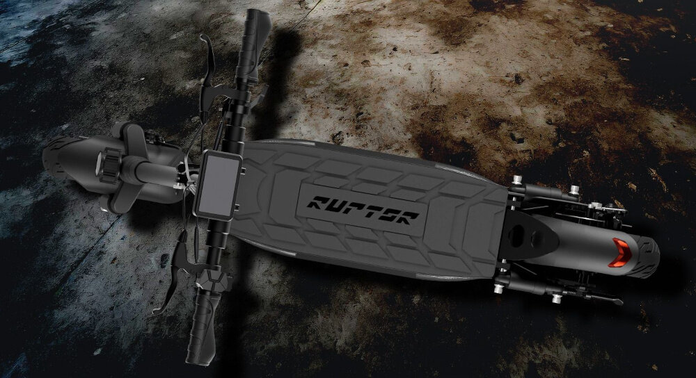 Widok z góry na czarną hulajnogę elektryczną z napisem \'RUPTOR\' na platformie. Tło jest ciemne i nierówne, przypominające betonową powierzchnię.