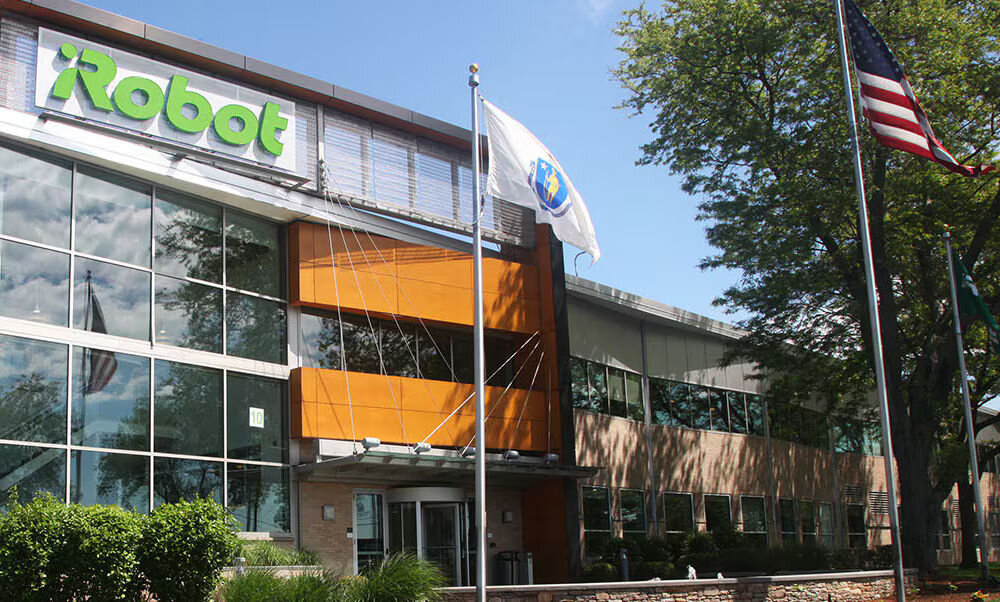 Budynek z dużymi oknami i logo \'iRobot\' na fasadzie. Przed budynkiem znajdują się flagi na masztach.
