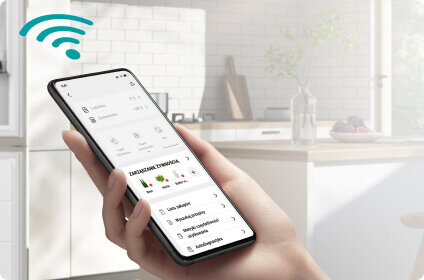 Osoba trzyma smartfon z aplikacją do zarządzania lodówką, w tle widoczna jest kuchnia z białymi szafkami. W lewym górnym rogu znajduje się symbol Wi-Fi.