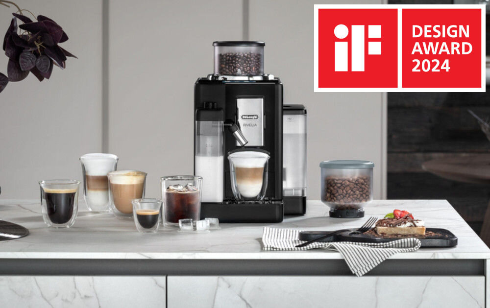 Na blacie kuchennym stoi czarny ekspres do kawy z logo Delonghi Rivelia, otoczony różnymi filiżankami z kawą. W prawym górnym rogu znajduje się czerwony znak z napisem \'iF DESIGN AWARD 2024\'.