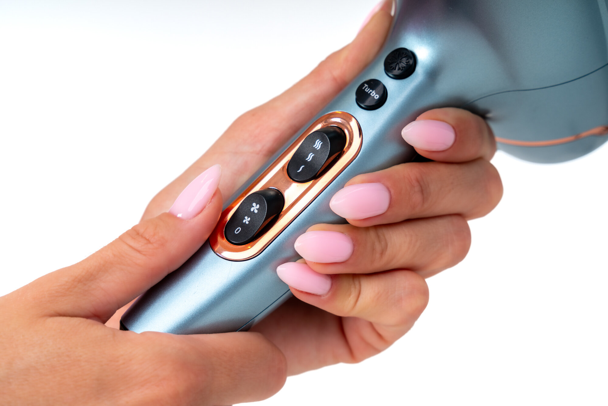 Osoba trzyma suszarkę do włosów w kolorze niebieskim z widocznymi przyciskami: \'Turbo\', symbolem nawiewu i temperatury. Suszarka ma elementy w kolorze miedzianym.