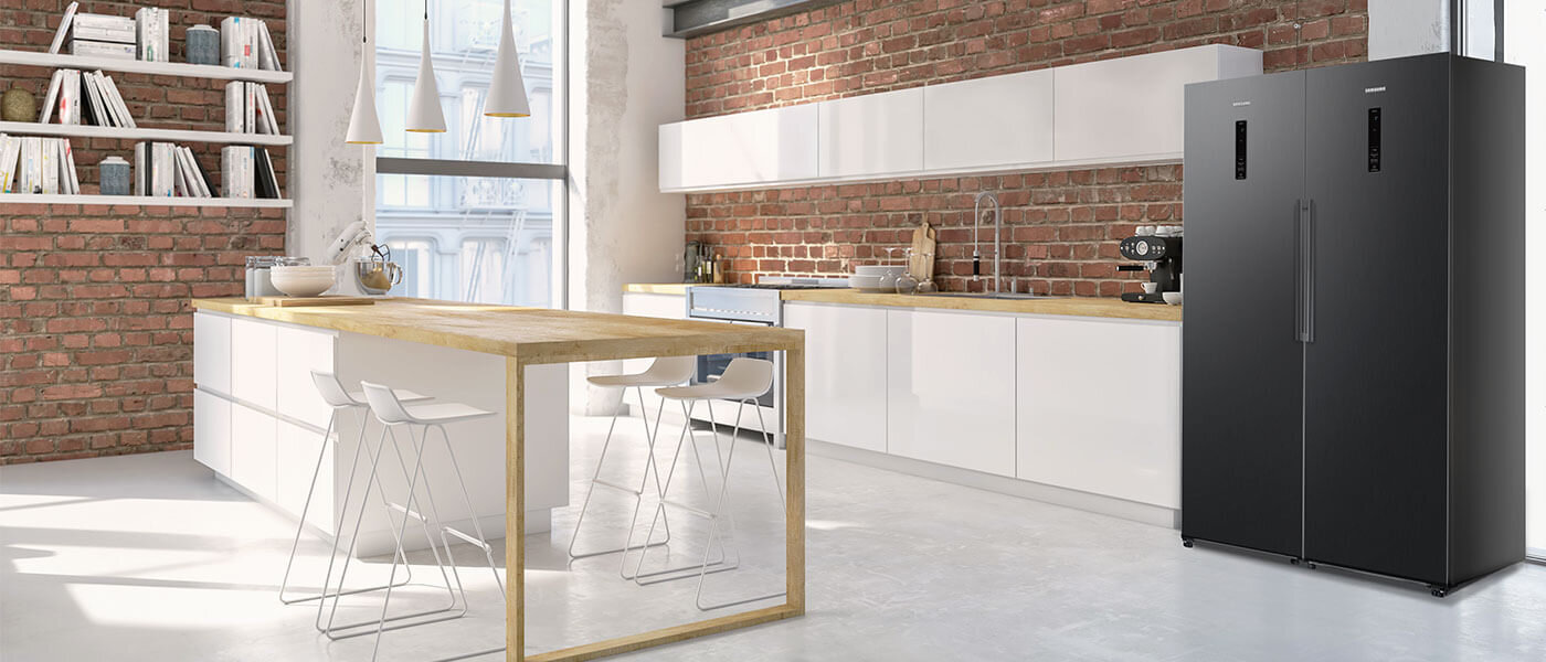 Nowoczesna kuchnia z ceglaną ścianą, białymi szafkami i drewnianym blatem. Po prawej stronie stoi grafitowa lodówka z logo Samsung.