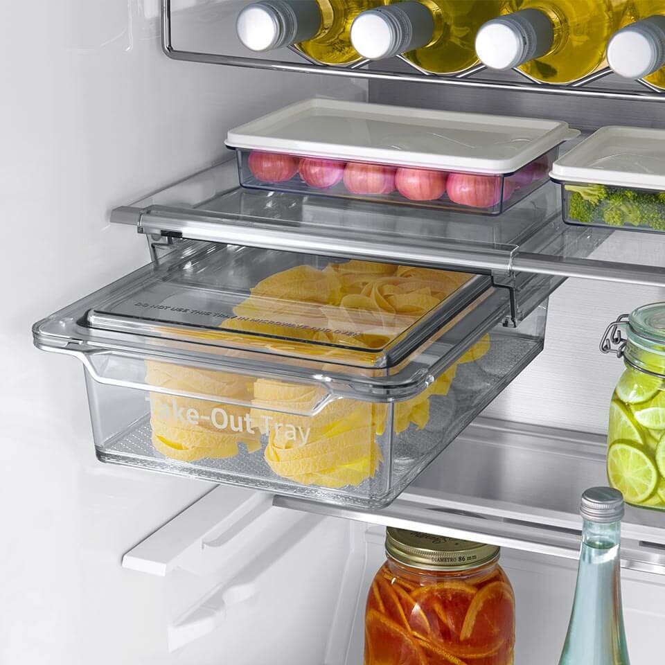 Wnętrze lodówki z widocznymi półkami, na których znajdują się butelki, pojemniki z jedzeniem oraz słoiki. Na jednym z pojemników widoczny jest napis \'Take-Out Tray\'.