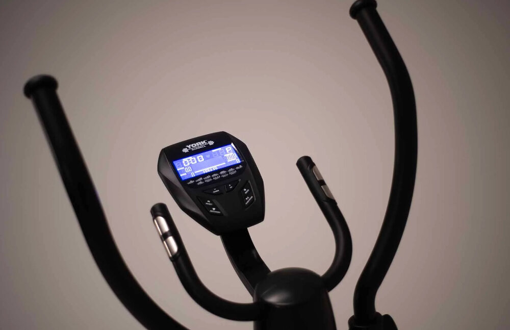 Na zdjęciu widoczny jest panel sterowania orbitreka z wyświetlaczem LCD, na którym znajdują się różne dane treningowe. Na panelu widnieje logo \'YORK FITNESS\'.