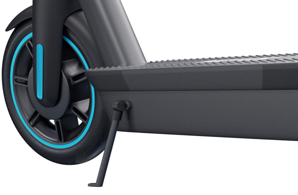 Obraz przedstawia fragment szarej hulajnogi elektrycznej z widocznym kołem i podnóżkiem. Koło ma niebieski akcent, a podnóżek jest rozłożony.