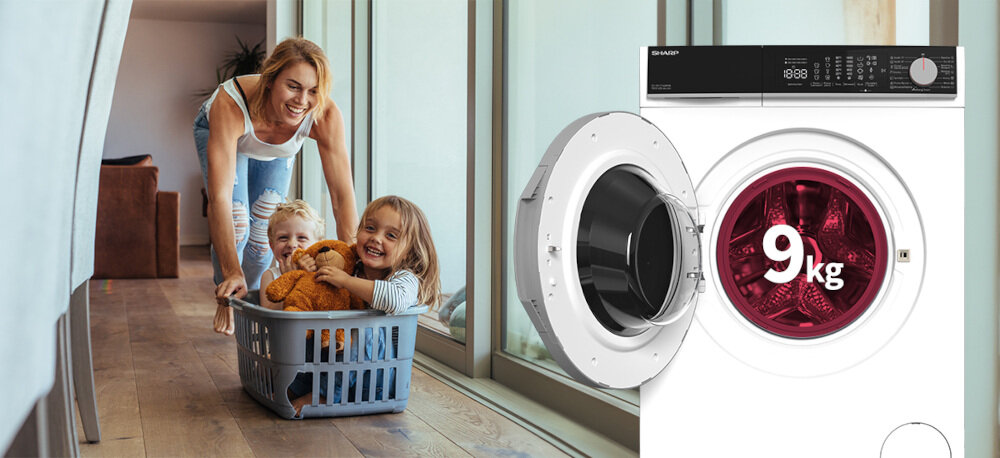 Na obrazie widoczna jest pralka z otwartymi drzwiami, na których widnieje napis \'9 kg\'. Obok pralki znajduje się kobieta pchająca kosz z dwójką dzieci w środku.
