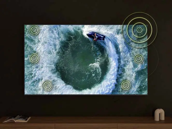 Telewizor wyświetla dynamiczną scenę z widokiem z góry na osobę na skuterze wodnym, tworzącą wir w wodzie. Na ekranie widoczne są okrągłe symbole sugerujące efekty dźwiękowe.