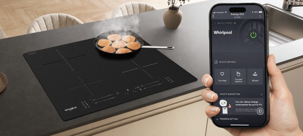 PŁYTA WHIRLPOOL MWS2260PCPNEBM Płyta indukcyjna zamontowana w wyspie kuchennej, a na jednym z pól smażą się kotlety. Na pierwszym planie widoczny jest smartfon z aplikacją Whirlpool do sterowania urządzeniem homewhiz sterowanie smart zdalne gotowanie kontrola płyty aplikacja mobilna