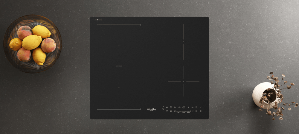 PŁYTA WHIRLPOOL MWS2260PCPNEBM Widok z góry na płytę indukcyjną osadzoną w blacie, obok misy z owocami i dekoracji. Układ pól grzewczych jest równomiernie rozplanowany 9 poziomów mocy slider sterowanie flexispace łatwy montaż ergonomia