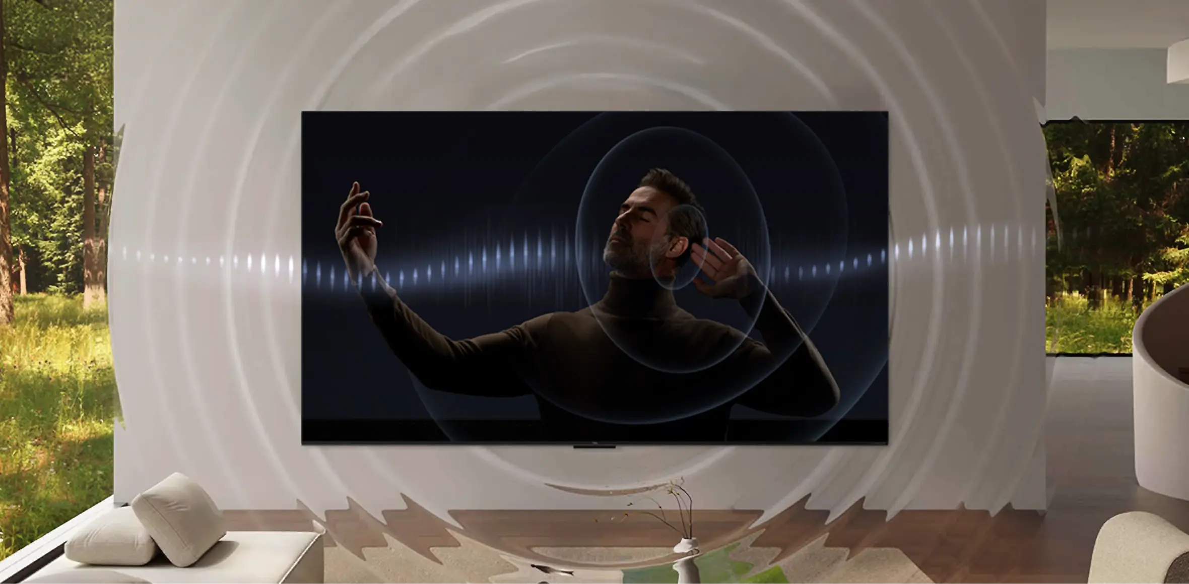 Telewizor wyświetla obraz mężczyzny z zamkniętymi oczami, otoczonego falami dźwiękowymi. W tle widoczny jest las za dużym oknem.