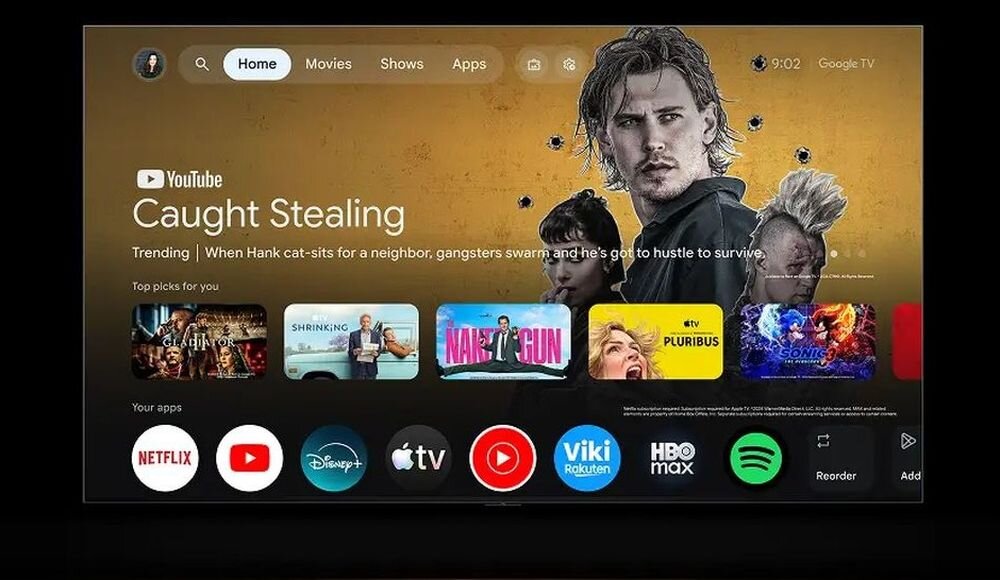 Ekran telewizora wyświetla interfejs Google TV z aplikacjami takimi jak Netflix, Disney+, Apple TV, YouTube i inne. Na ekranie widoczny jest film \'Caught Stealing\' oraz różne ikony aplikacji w dolnej części.