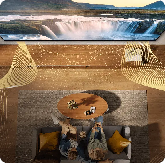 Widok z góry na parę na kanapie; ilustracja złotych fal wokół telewizora symbolizuje dźwięk przestrzenny Dolby Atmos