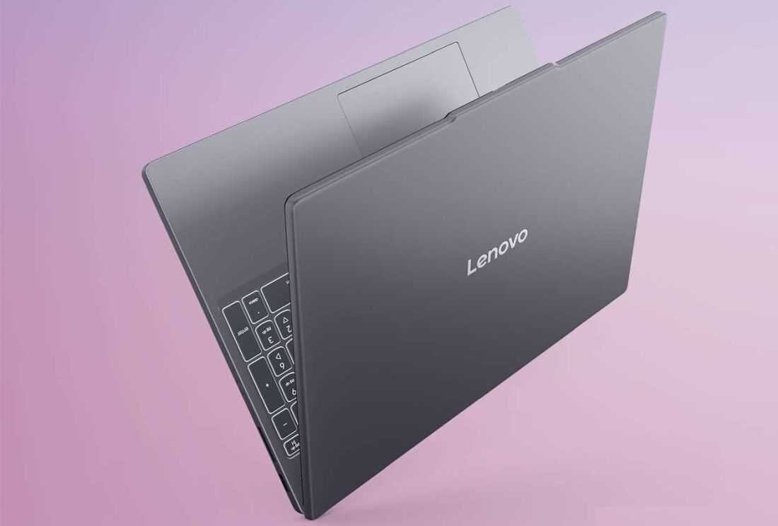 Na obrazie widoczny jest laptop w kolorze szarym z logo \'Lenovo\' na pokrywie. Laptop jest częściowo otwarty, a tło jest w odcieniach różu.