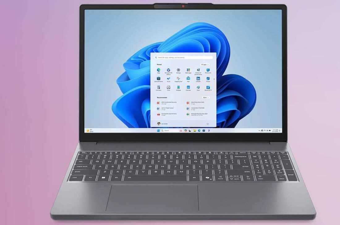 Laptop z otwartym ekranem wyświetlającym system Windows 11 z ikonami aplikacji. Klawiatura jest widoczna, a tło jest w kolorze różowym.