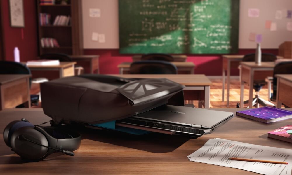 Na biurku w klasie leży otwarty plecak z wystającym laptopem, obok znajdują się słuchawki i dokumenty. W tle widać tablicę z zapisanymi wzorami matematycznymi oraz puste ławki.