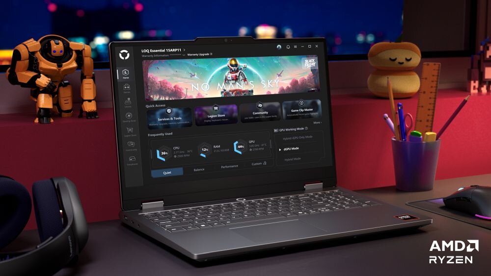 Na biurku znajduje się otwarty laptop z wyświetlonym na ekranie interfejsem gry \'No Man\'s Sky\'. Obok laptopa widoczne są słuchawki, figurka robota i przybory biurowe, a w prawym dolnym rogu ekranu znajduje się logo \'AMD Ryzen\'.