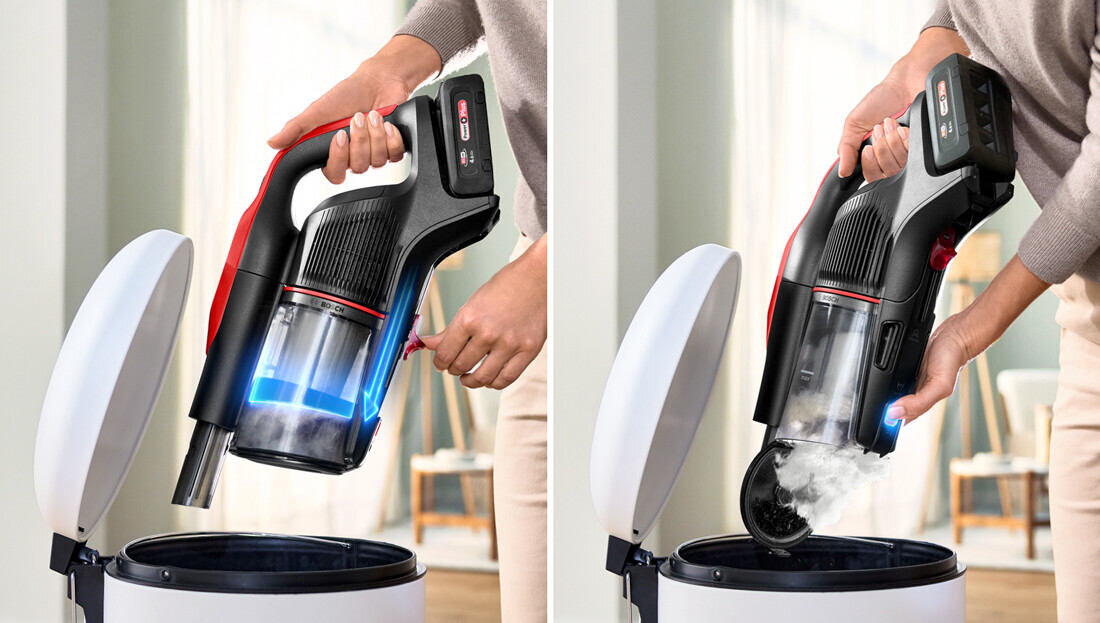 Osoba trzyma odkurzacz pionowy nad otwartym koszem na śmieci, pokazując proces opróżniania pojemnika na kurz. Odkurzacz ma czarną obudowę z czerwonymi akcentami i przezroczystym pojemnikiem na kurz.