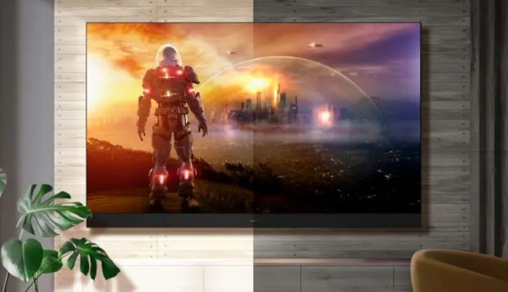 Telewizor wyświetla obraz z futurystycznym miastem i postacią w zbroi na tle zachodzącego słońca. W pomieszczeniu obok telewizora znajduje się roślina doniczkowa.