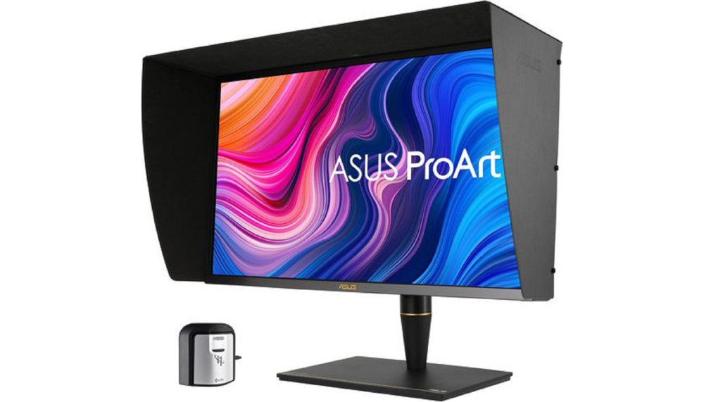 Monitor z kolorowym wyświetlaczem i napisem \'ASUS ProArt\', wyposażony w osłonę przeciwsłoneczną. Obok monitora znajduje się małe urządzenie kalibracyjne.