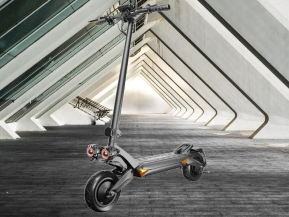 Czarna hulajnoga elektryczna z dużymi kołami i amortyzacją stoi na tle nowoczesnej architektury z białymi, skośnymi filarami. Hulajnoga ma dwa reflektory z przodu i solidną konstrukcję.