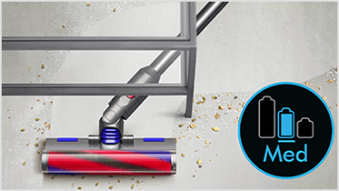 Odkurzacz z czerwono-niebieską szczotką zbiera drobinki z podłogi. Obok widoczna jest ikona z trzema bateriami i napisem \'Med\'.