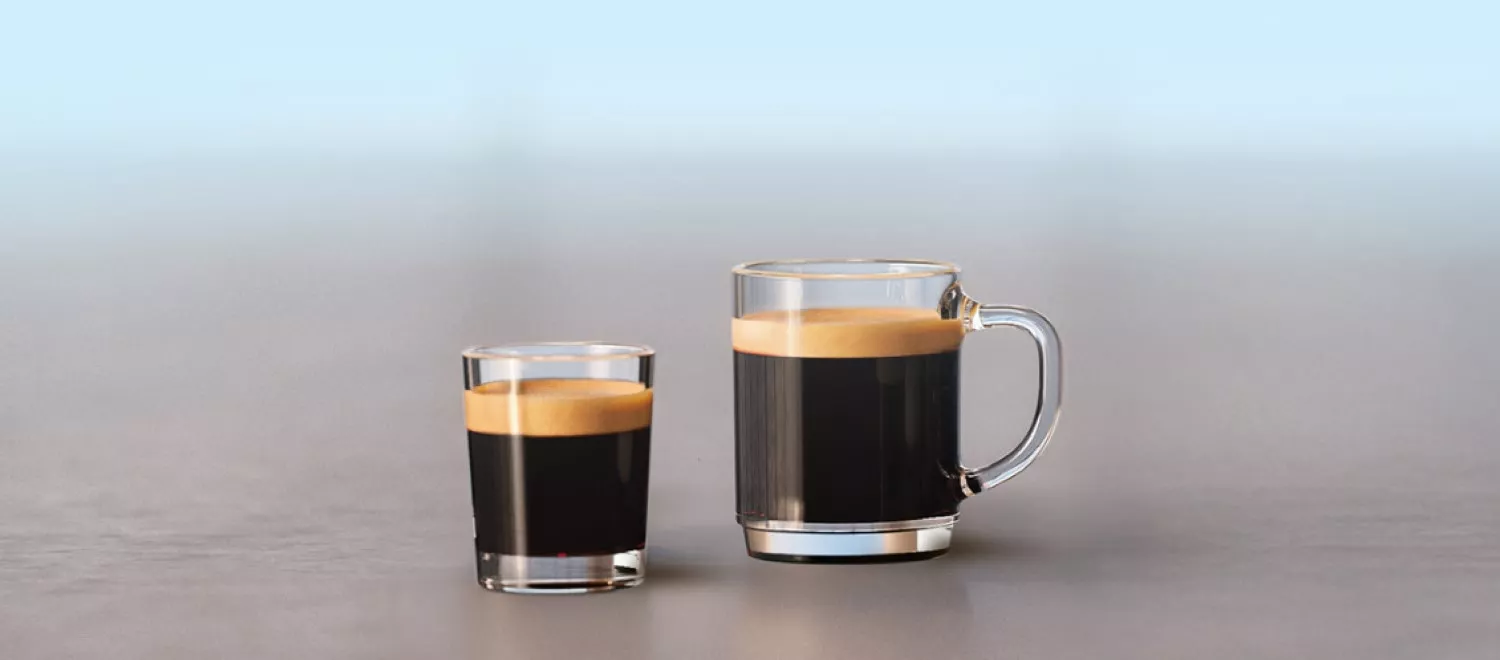 Na obrazie znajdują się dwie szklanki z czarną kawą, jedna mniejsza i jedna większa, obie z pianką na wierzchu. Tło jest jednolite i rozmyte.