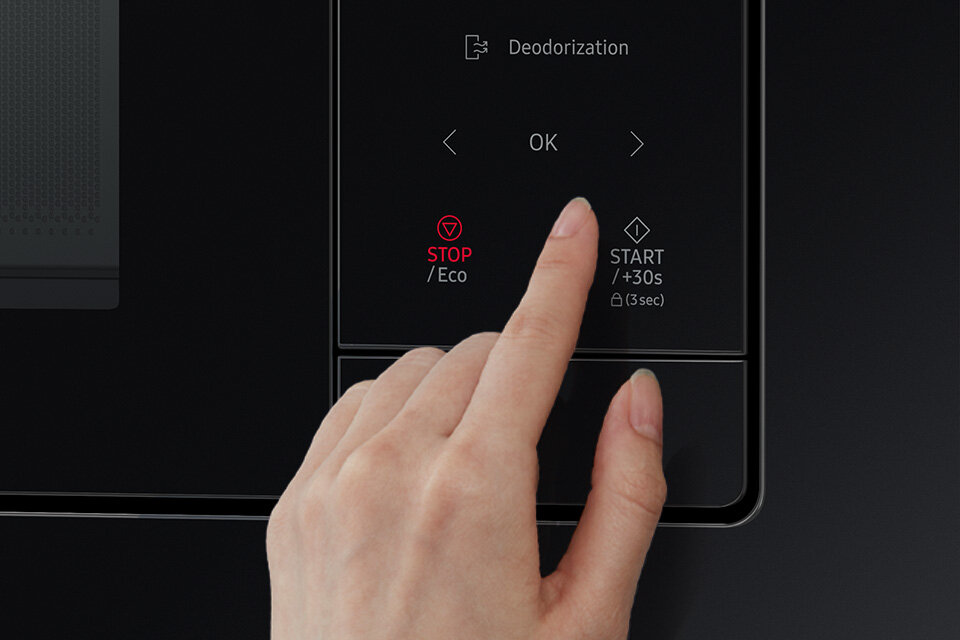 Panel sterowania kuchenki mikrofalowej z przyciskami: \'Deodorization\', \'STOP/Eco\', \'START/+30s (3 sec)\', oraz strzałkami i przyciskiem \'OK\'. Dłoń naciska przycisk \'OK\'.
