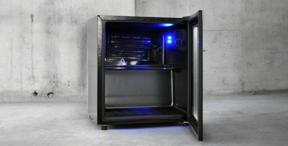 Otwarta witryna chłodnicza z niebieskim oświetleniem wewnętrznym, ustawiona na betonowej podłodze. Wnętrze jest puste, a drzwi są uchylone.