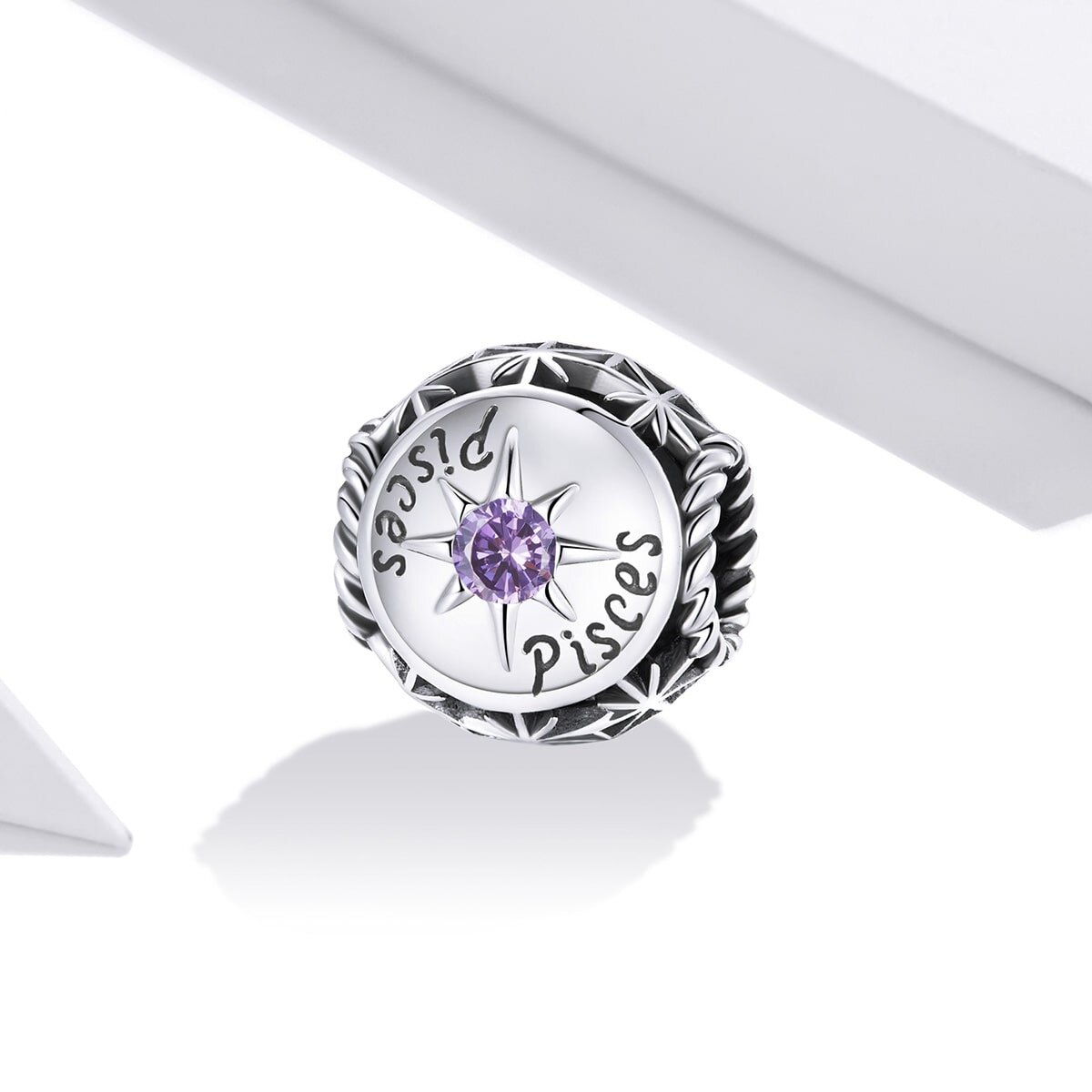 Srebrny charms z napisem \'Pisces\' i fioletowym kamieniem w centrum, otoczony ozdobnym wzorem. Produkt jest przedstawiony na białym tle.