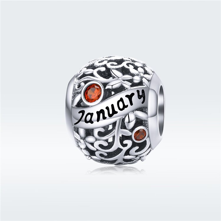 Srebrny charms z ażurowym wzorem, ozdobiony czerwonymi kamieniami i napisem \'January\'.