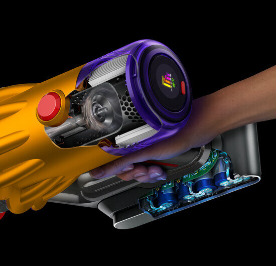 Ręka trzyma odkurzacz z widocznym przekrojem ukazującym wnętrze urządzenia, w tym elementy mechaniczne i elektroniczne. Odkurzacz ma żółto-fioletową obudowę z wyświetlaczem na końcu.