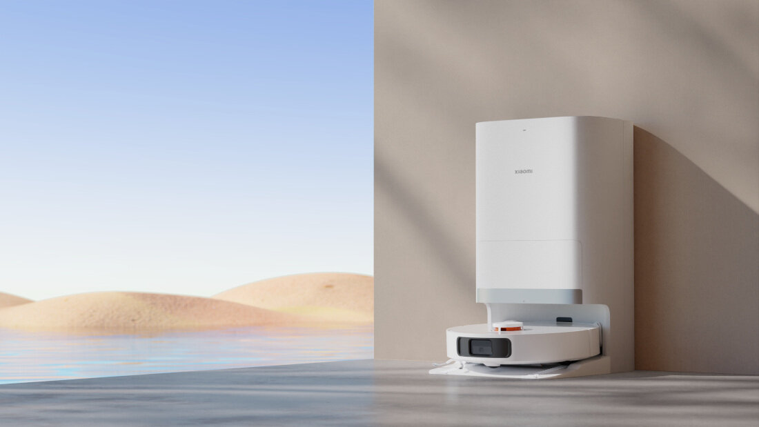 Na obrazie widoczny jest biały robot sprzątający z dokiem ładującym na tle pustynnego krajobrazu. Na urządzeniu znajduje się logo \'XIAOMI\'.