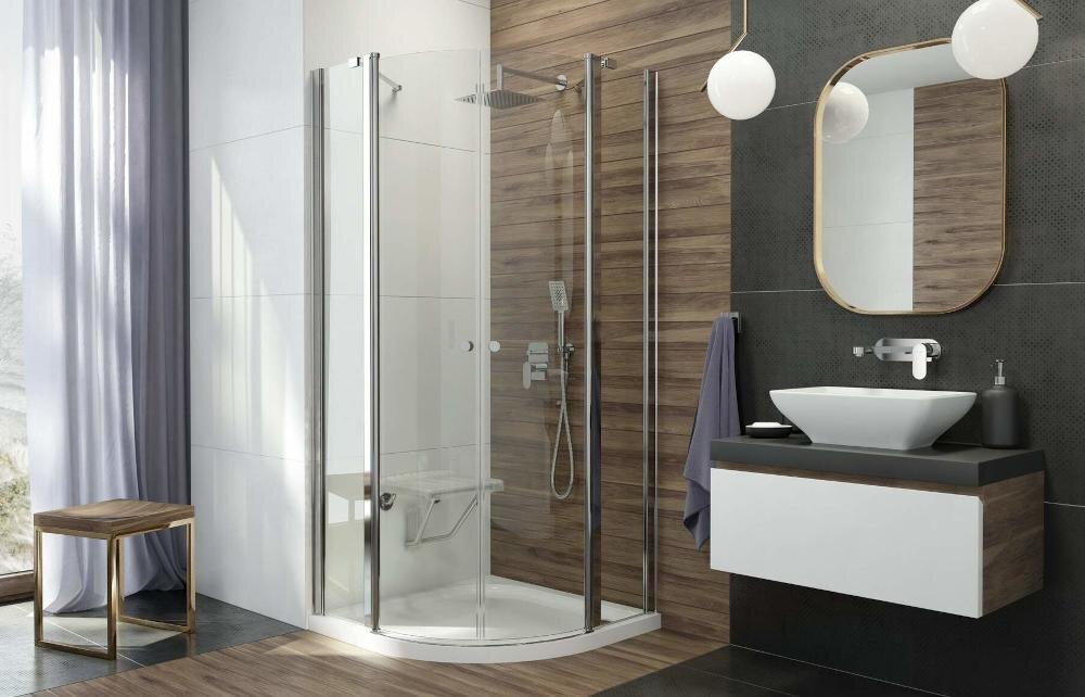 Łazienka z kabiną prysznicową z przezroczystymi drzwiami i deszczownicą. Obok znajduje się umywalka z lustrem i wiszącą lampą.