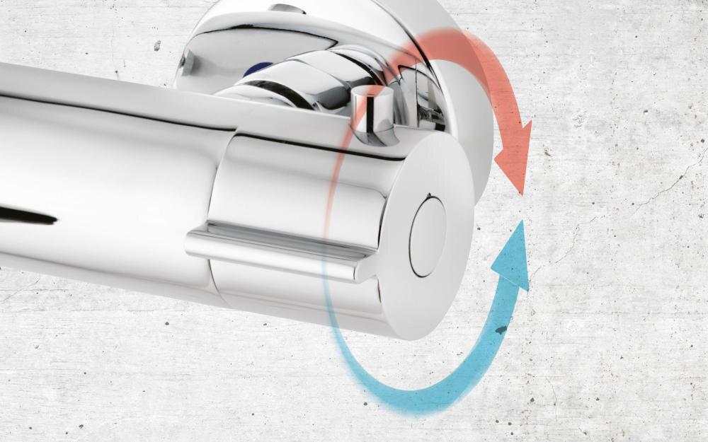 Chromowana część zestawu prysznicowego z widocznymi strzałkami w kolorach czerwonym i niebieskim wskazującymi kierunek obrotu. Tło jest jasne i teksturowane.