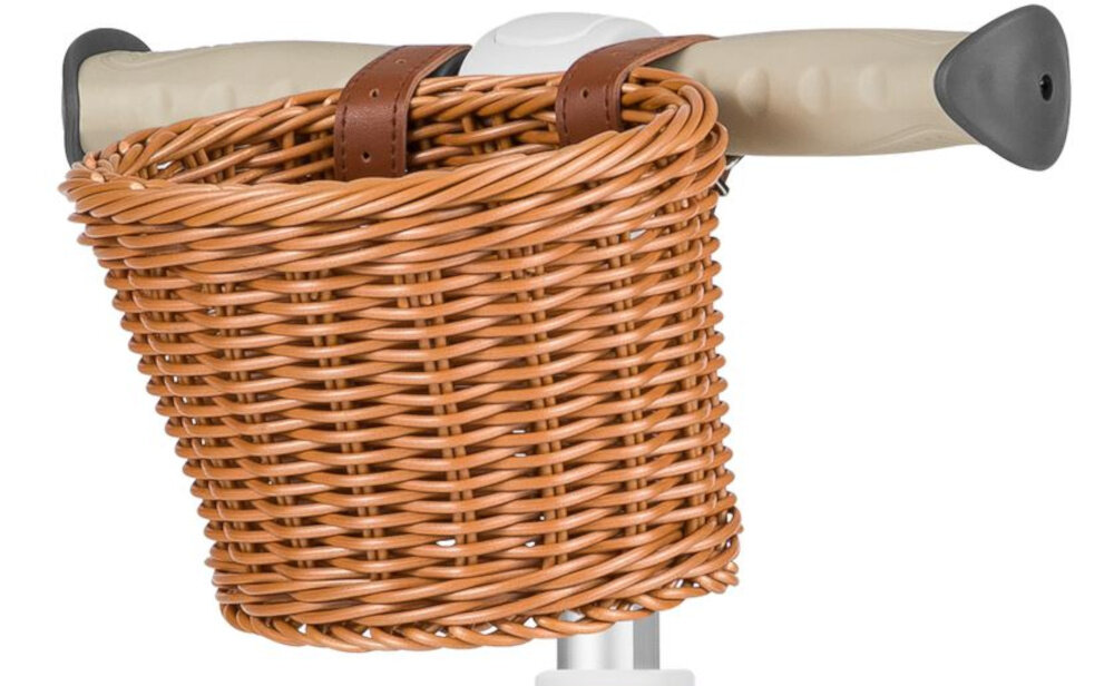 Na obrazie widoczny jest koszyk wiklinowy przymocowany do kierownicy hulajnogi. Kierownica ma beżowe uchwyty z czarnymi końcówkami.
