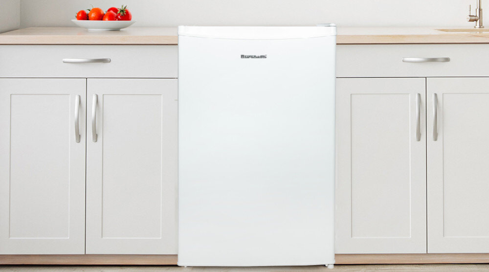Biała lodówka z logo \'RAVANSON\' stoi pomiędzy szafkami kuchennymi. Na blacie obok znajduje się talerz z pomidorami.