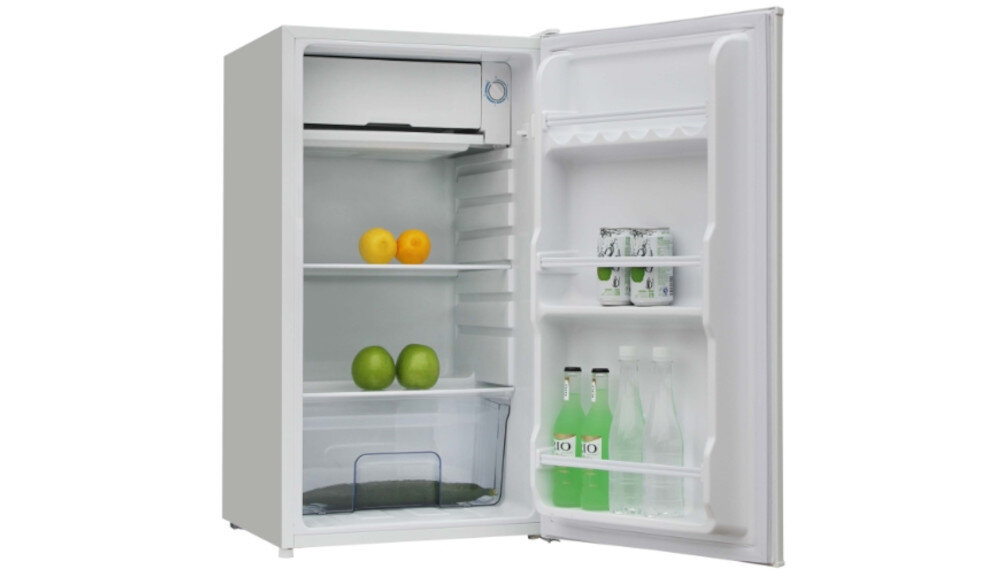 Otwarta biała lodówka z widocznymi półkami, na których znajdują się owoce, puszki i butelki. Wewnątrz lodówki są dwie pomarańcze, dwie zielone jabłka, dwie puszki oraz trzy butelki z napojami.