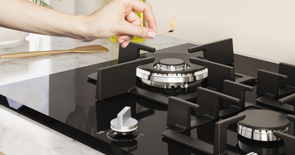 PŁYTA BOSCH PNH6B6K40 Na zdjęciu widać rękę z zapałką nad centralnym palnikiem płyty gazowej, gotową do rozpalenia ognia. Palniki otoczone są masywnymi rusztami, a na pierwszym planie widoczny jest srebrny, obrócony pokrętłem regulator gazu automatyczne odcięcie gazu czujnik bezpieczeństwa ochrona przed zalaniem ochrona przed podmuchem pewne gotowanie niezawodna ochrona